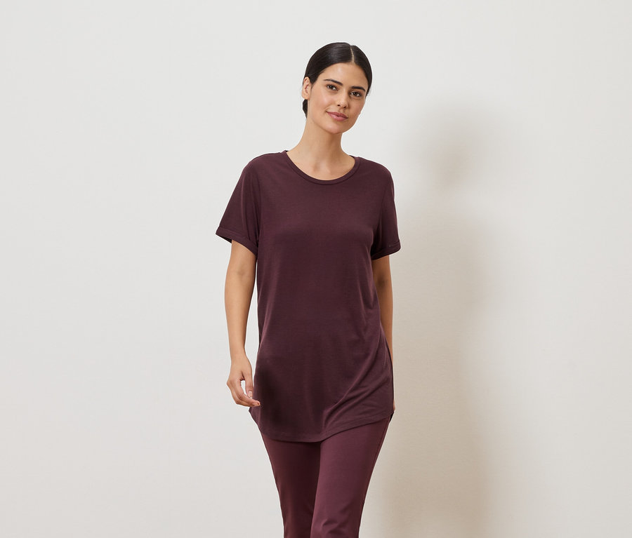 Femme portant un t-shirt bordeaux et un legging sur fond neutre.