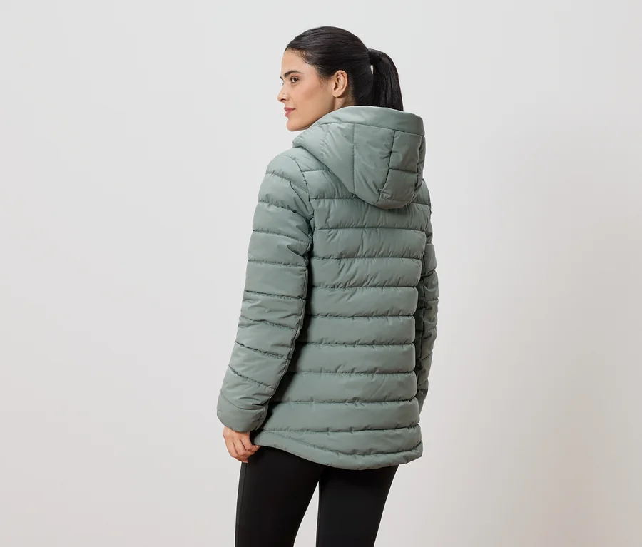 Une femme portant une queue de cheval, vue de dos, porte une veste matelassée vert clair à capuche et un legging noir.