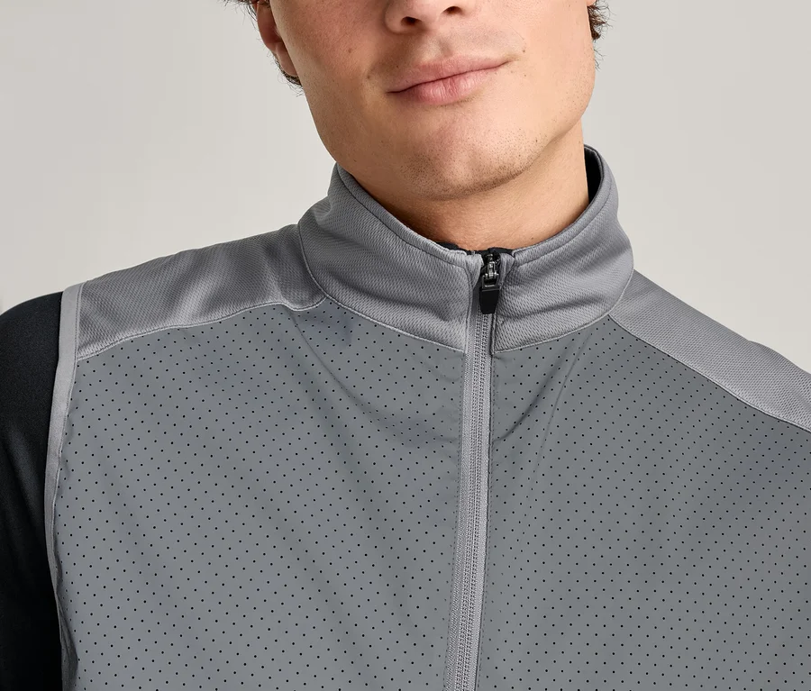 Gros plan d'un homme portant un gilet gris zippé sur un t-shirt noir à manches longues.