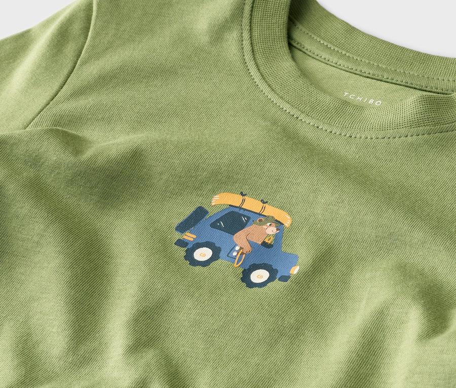 T-shirt vert avec un ours conduisant une voiture bleue avec des bagages sur le toit.