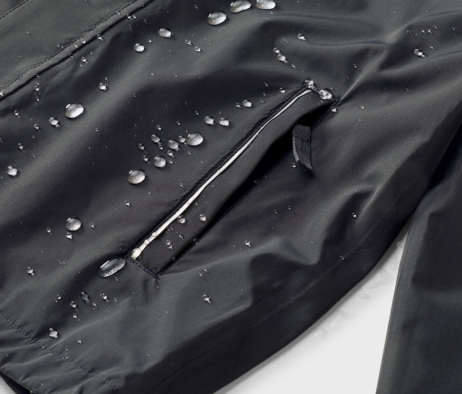 Gros plan d'une veste noire avec une surface imperméable et une poche zippée avec une bordure blanche, sur laquelle on peut voir des gouttes d'eau.