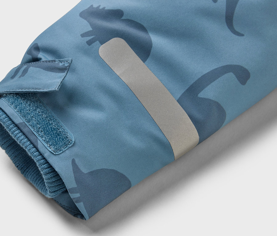 Manche d'une veste bleu clair avec des silhouettes de dinosaures plus foncées, une fermeture velcro et une bande réfléchissante.