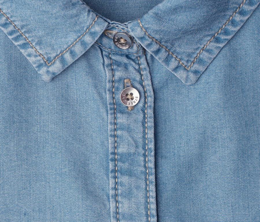 Gros plan d'une chemise en jean bleu clair avec un col et deux boutons argentés.