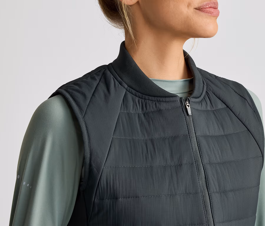 Femme portant un gilet matelassé gris sur un t-shirt vert à manches longues.