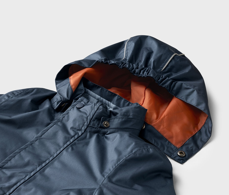 Gros plan d'un imperméable bleu foncé avec une capuche orange sur fond blanc.