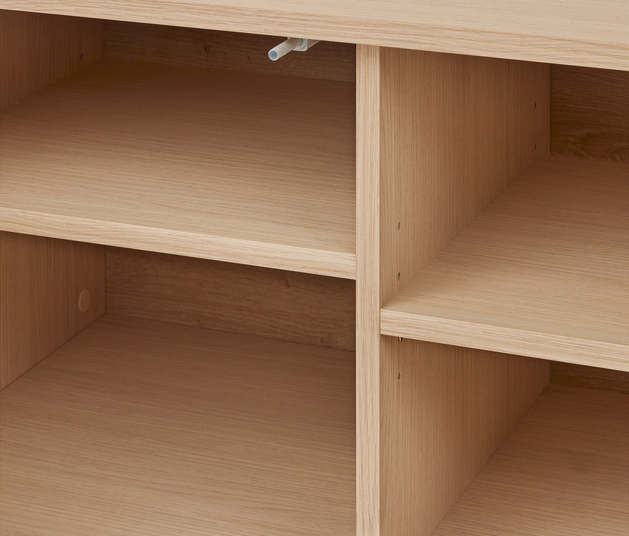Gros plan sur une étagère en bois clair avec plusieurs compartiments vides. Un passe-câble blanc est visible dans la section supérieure gauche.