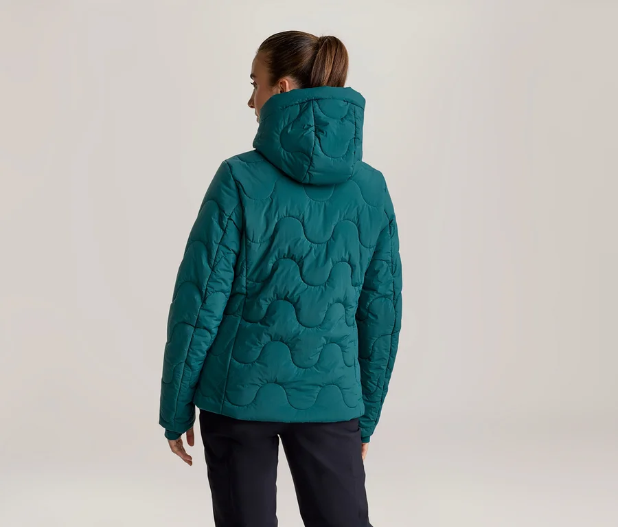 Personne vue de dos portant une veste matelassée turquoise à capuche avec des coutures ondulées, et un pantalon foncé.