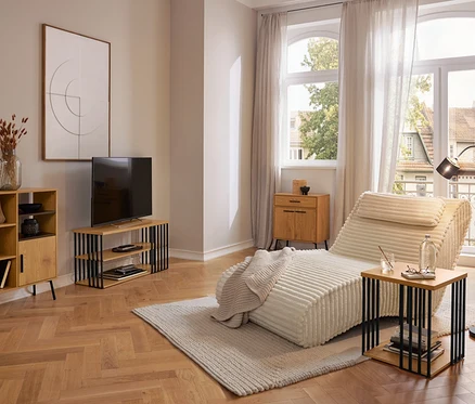 Salon moderne avec une méridienne crème sur un tapis clair, une armoire en bois, un meuble TV et une table d'appoint. De grandes fenêtres avec des rideaux donnent sur l'extérieur.
