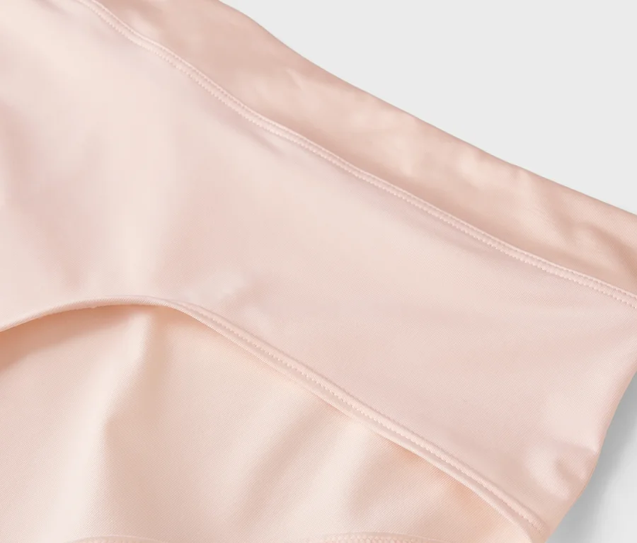 Gros plan d'un tissu rose pâle ou pêche avec des coutures visibles.