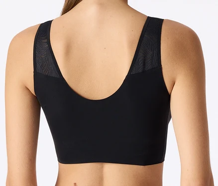 Vue de dos d'une personne portant une brassière de sport noire avec un décolleté en V et des empiècements en maille à motifs sur les épaules.