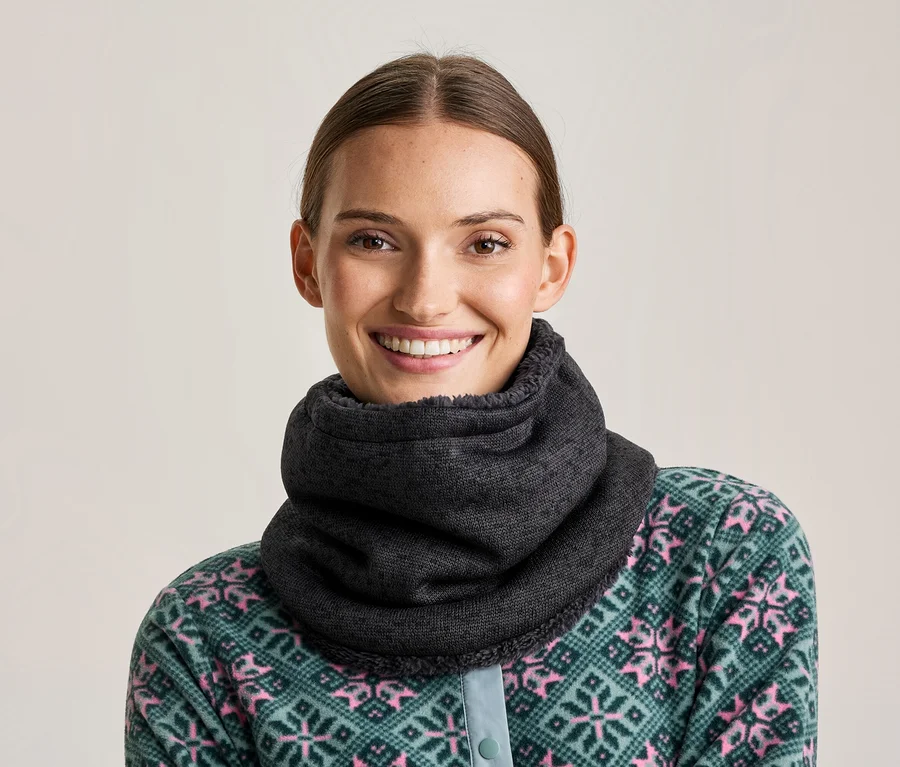 Femme souriante portant un cache-cou gris foncé et un haut en polaire à motifs vert et rose.