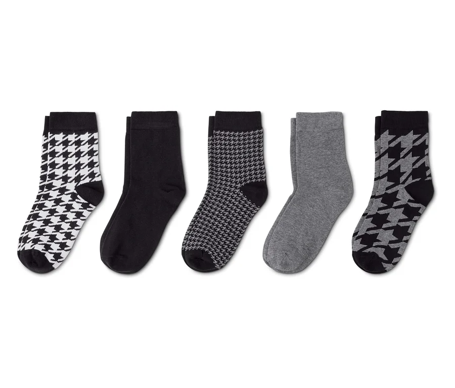 Cinq paires de chaussettes alignées: une paire blanche à motif pied-de-poule noir, une paire noire unie, une paire noire à petit motif pied-de-poule blanc, une paire grise unie et une paire grise à motif pied-de-poule noir.