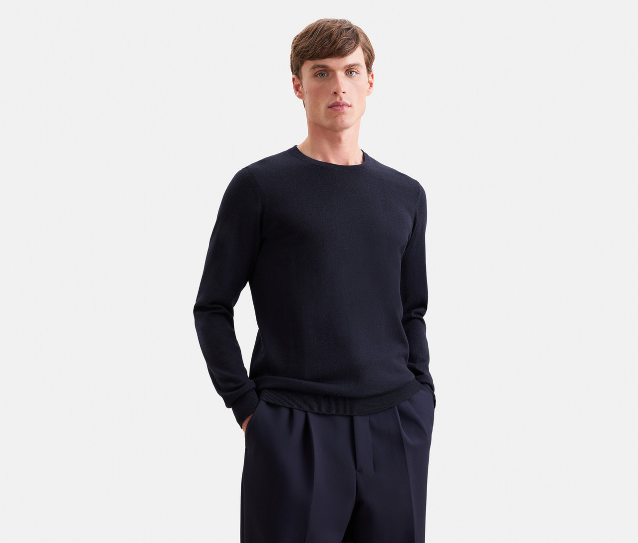 Homme portant un pull à manches longues bleu foncé et un pantalon bleu foncé, les mains dans les poches.