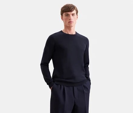 Homme portant un pull à manches longues bleu foncé et un pantalon bleu foncé, les mains dans les poches.