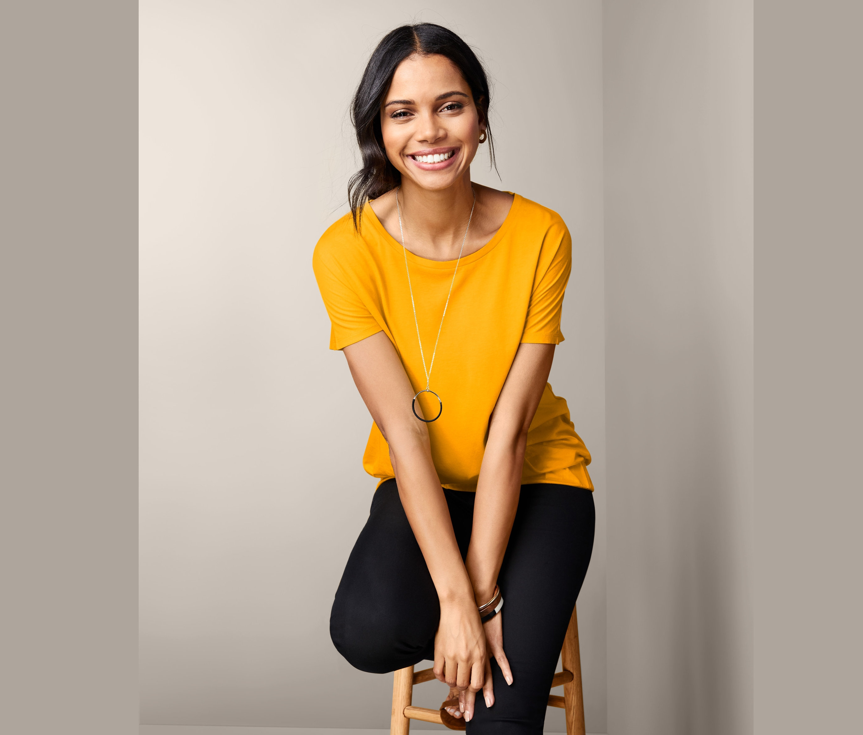 Une femme est assise sur un tabouret et porte un t-shirt manches courtes jaune.