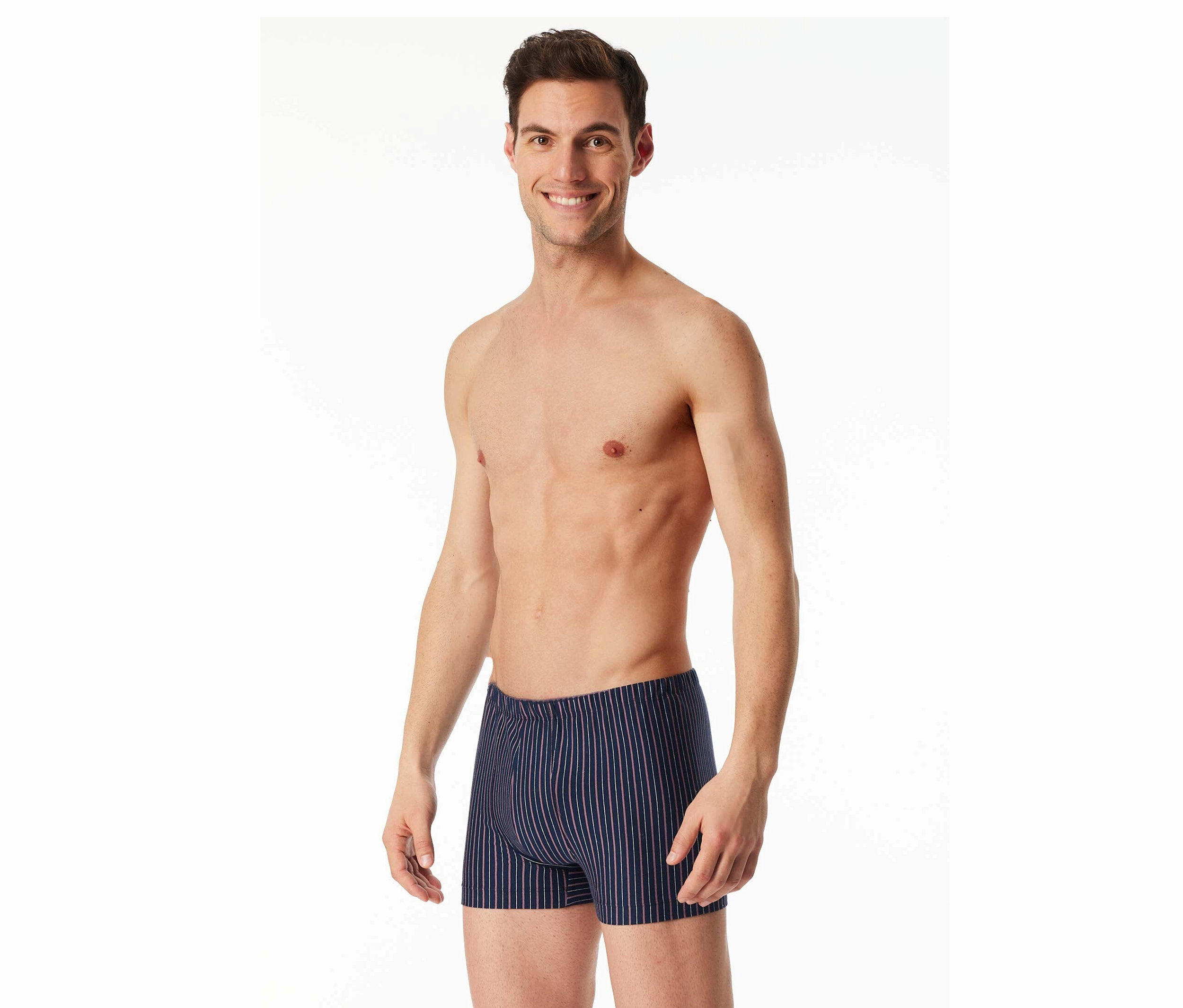 Un homme souriant torse nu porte un caleçon boxeur rayé sur fond blanc.