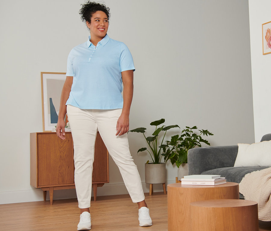 Femme posant en jean slim blanc crème, polo bleu clair et baskets en cuir velours blanches.