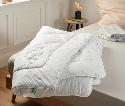 Une couette blanche irisette® greenline Duo en poil de chameau est posée sur un lit.