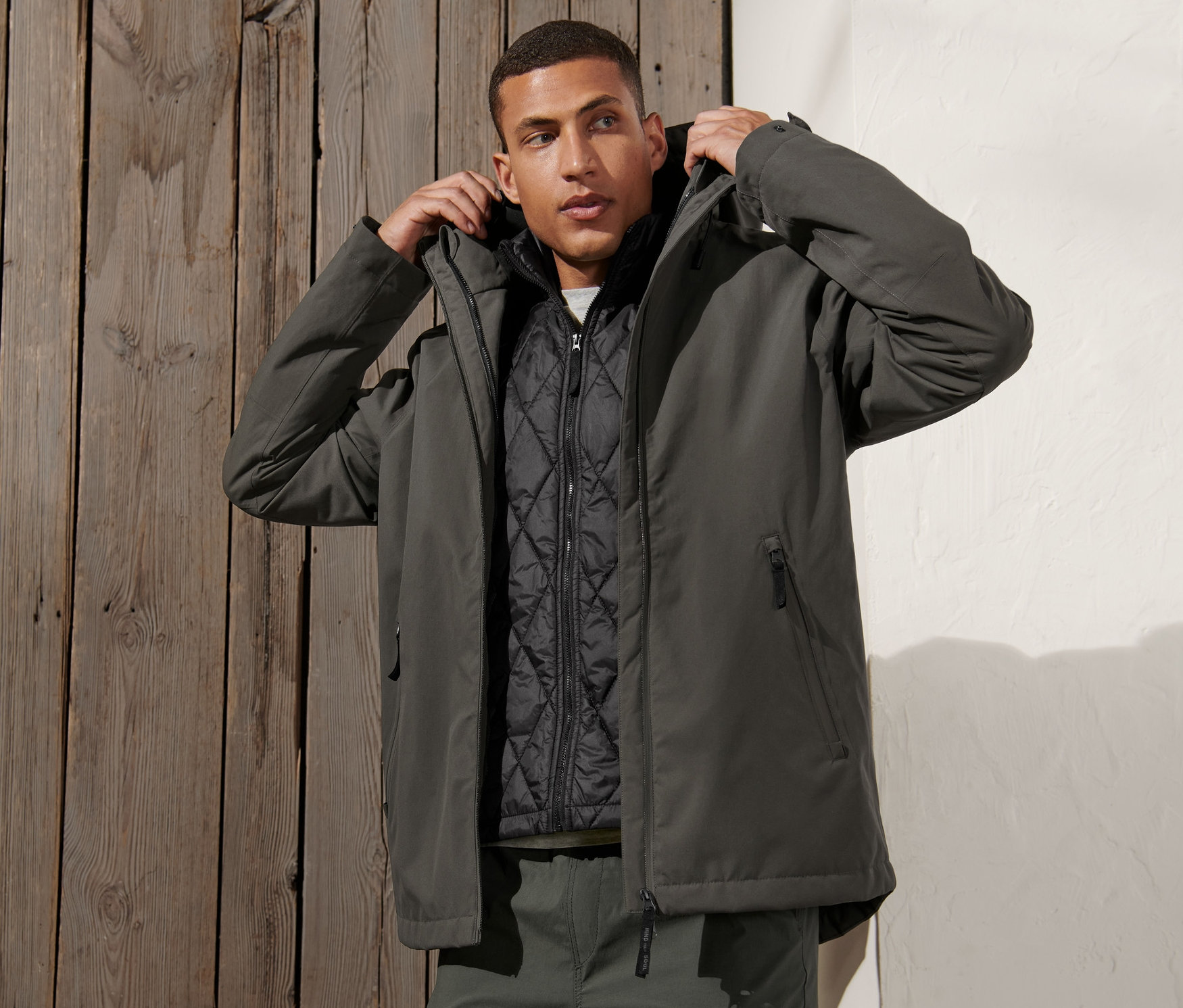 Un homme ajuste la capuche d'une veste d'extérieur 3 en 1 avec gilet, de couleur vert-gris.