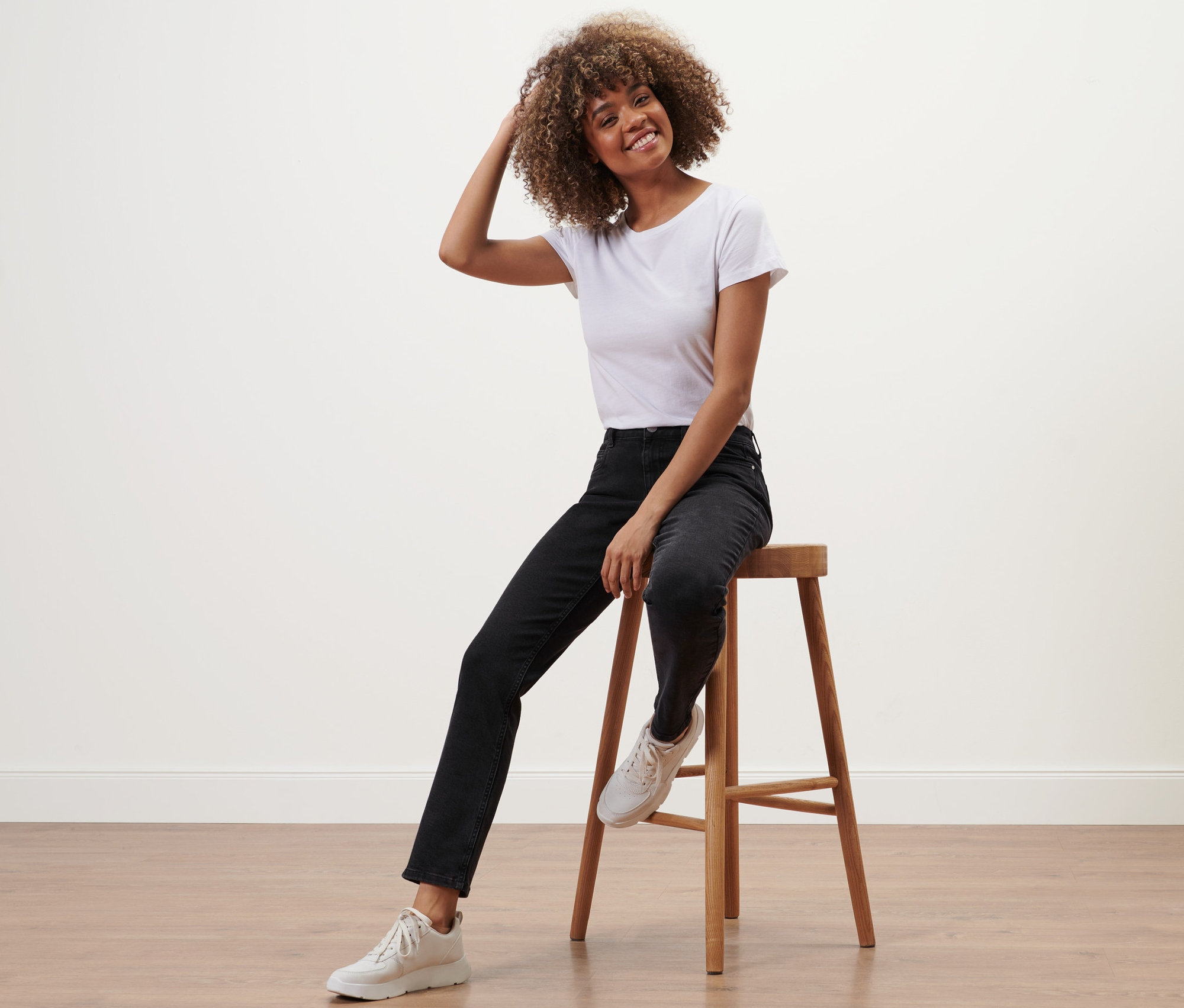 Une femme est assise sur un tabouret et porte un jean droit en denim «
Ajustement Juna
», noir.