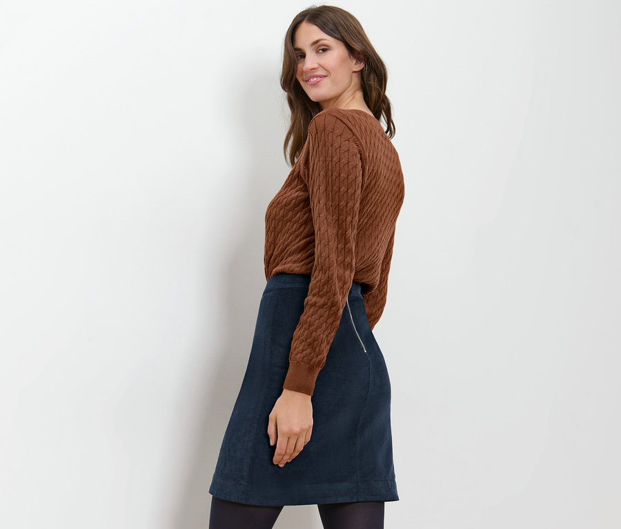 Une femme pose avec un pull marron et une jupe en velours bleu marine.