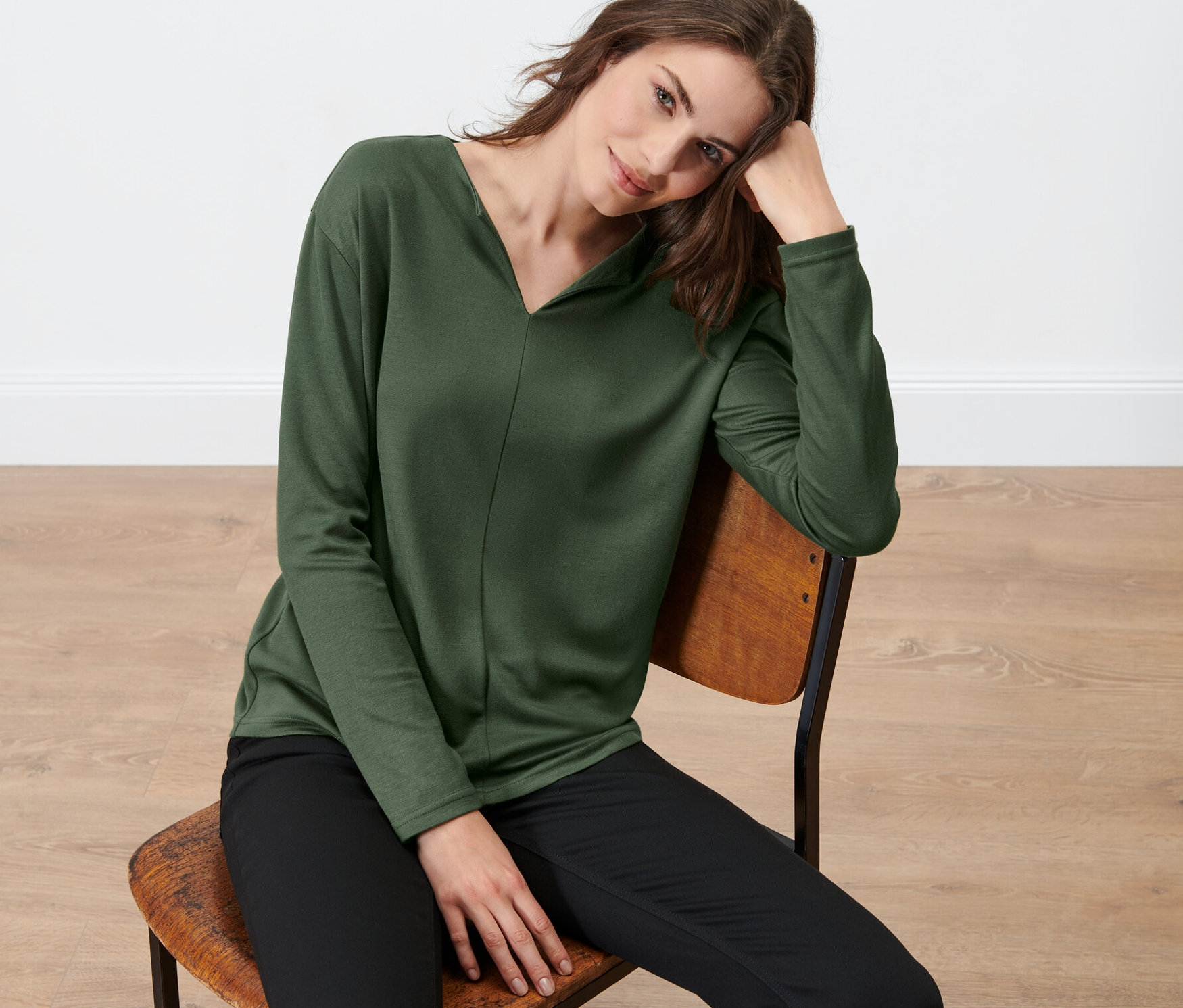 Femme assise sur une chaise portant une blouse vert foncé.