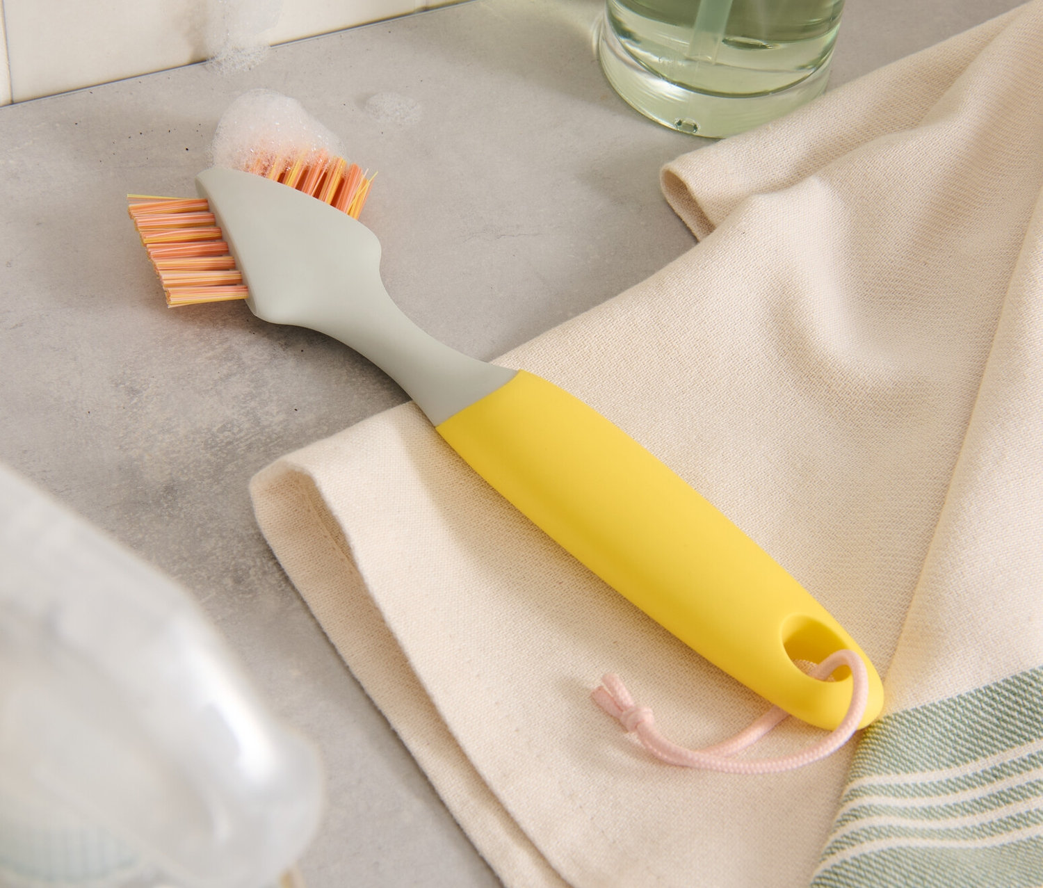 Une brosse de nettoyage pour joints repose sur un torchon à côté de bouteilles de nettoyage.