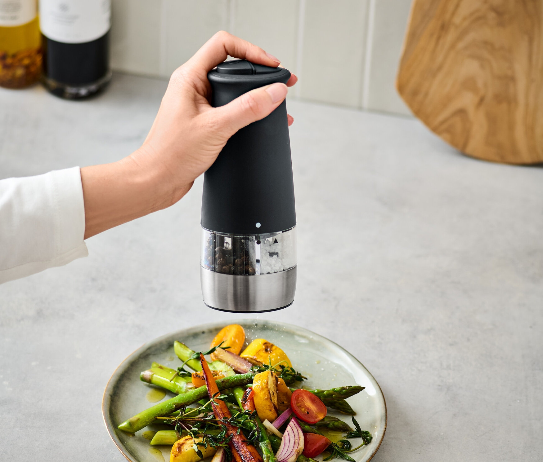 Une main utilise un moulin à sel et à poivre 2 en 1 électrique au-dessus d'une assiette de légumes.