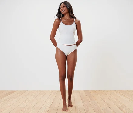 Une femme souriante porte un débardeur blanc et 5 Slips Magic Cut.