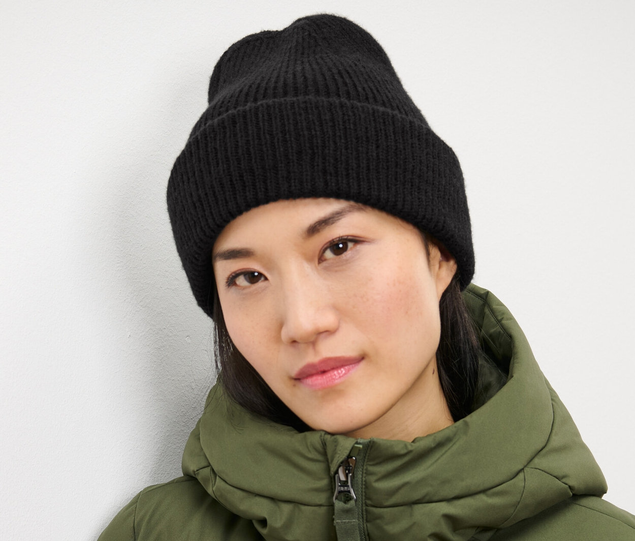 Une femme portant un bonnet en maille noir et une veste verte.