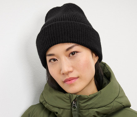 Une femme portant un bonnet en maille noir et une veste verte.