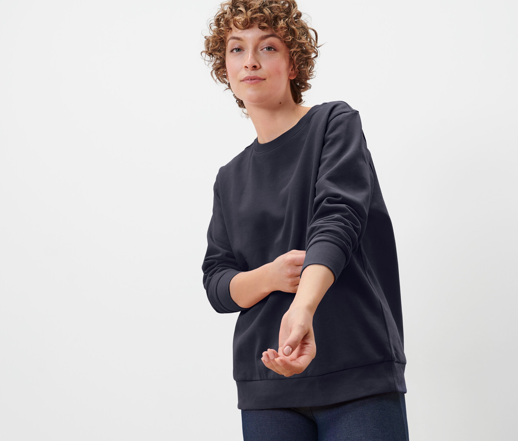 Une femme aux cheveux bouclés porte un sweat-shirt bleu foncé.