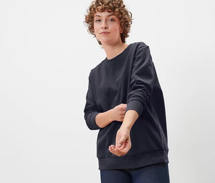 Une femme aux cheveux bouclés porte un sweat-shirt bleu foncé.