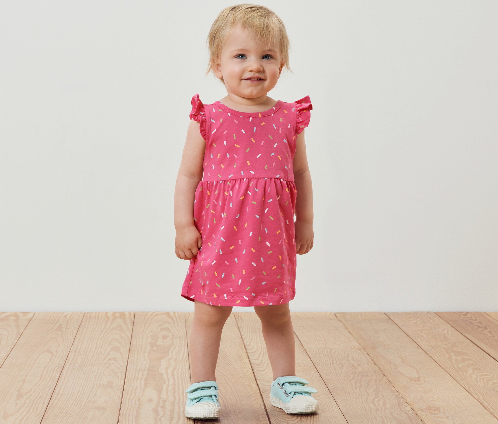 Petite fille souriante debout portant une robe en jersey rose.