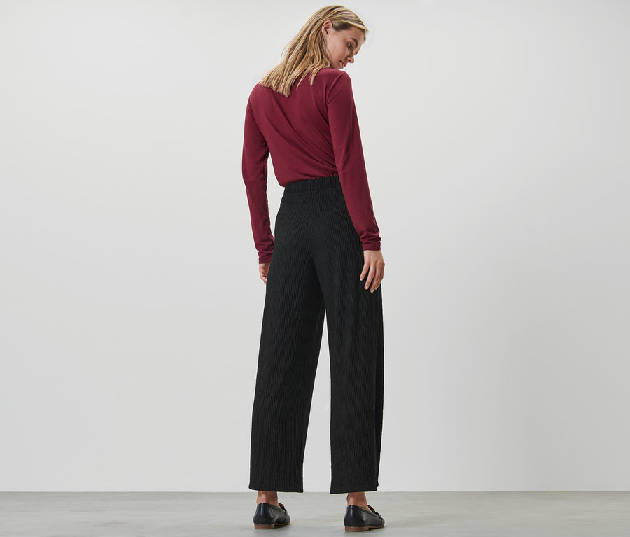 Une femme vue de dos portant un pantalon plissé noir.