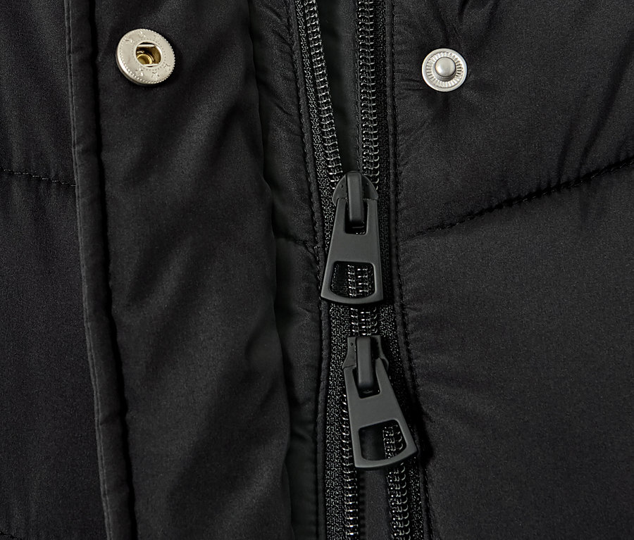 Gros plan sur un manteau matelassé à capuche noir, montrant la fermeture éclair et les boutons-pression.
