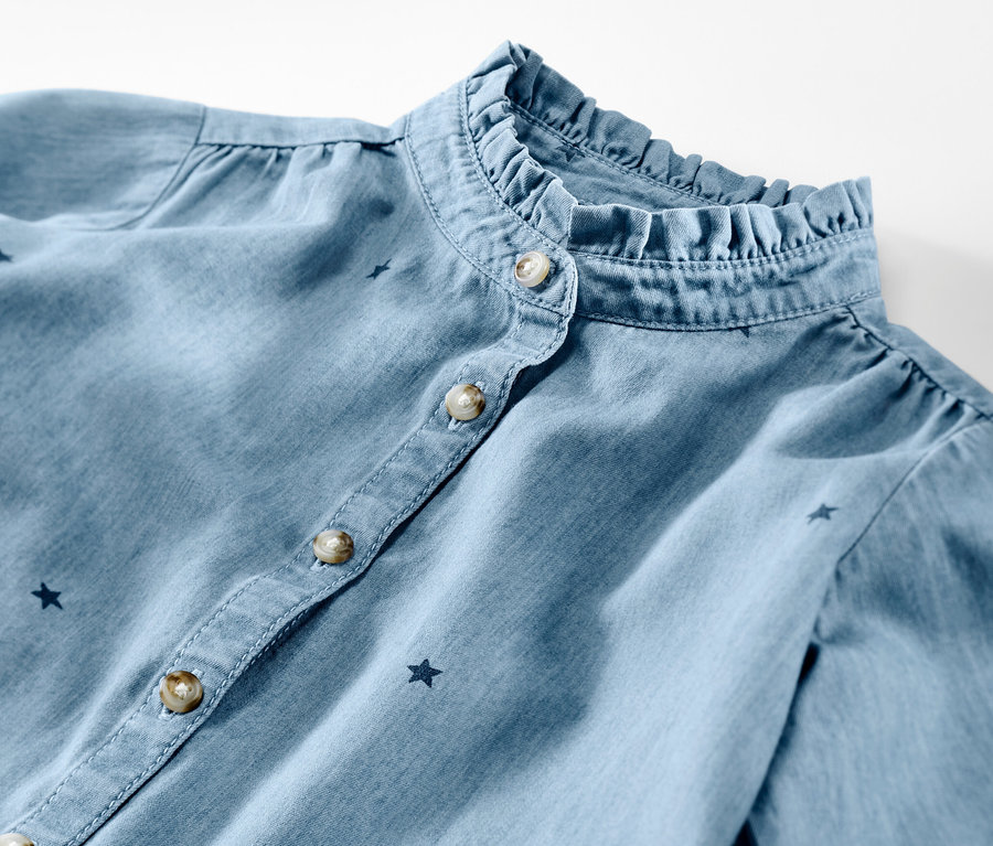 Gros plan sur une chemise en chambray pour enfant avec un col à volants et des étoiles.