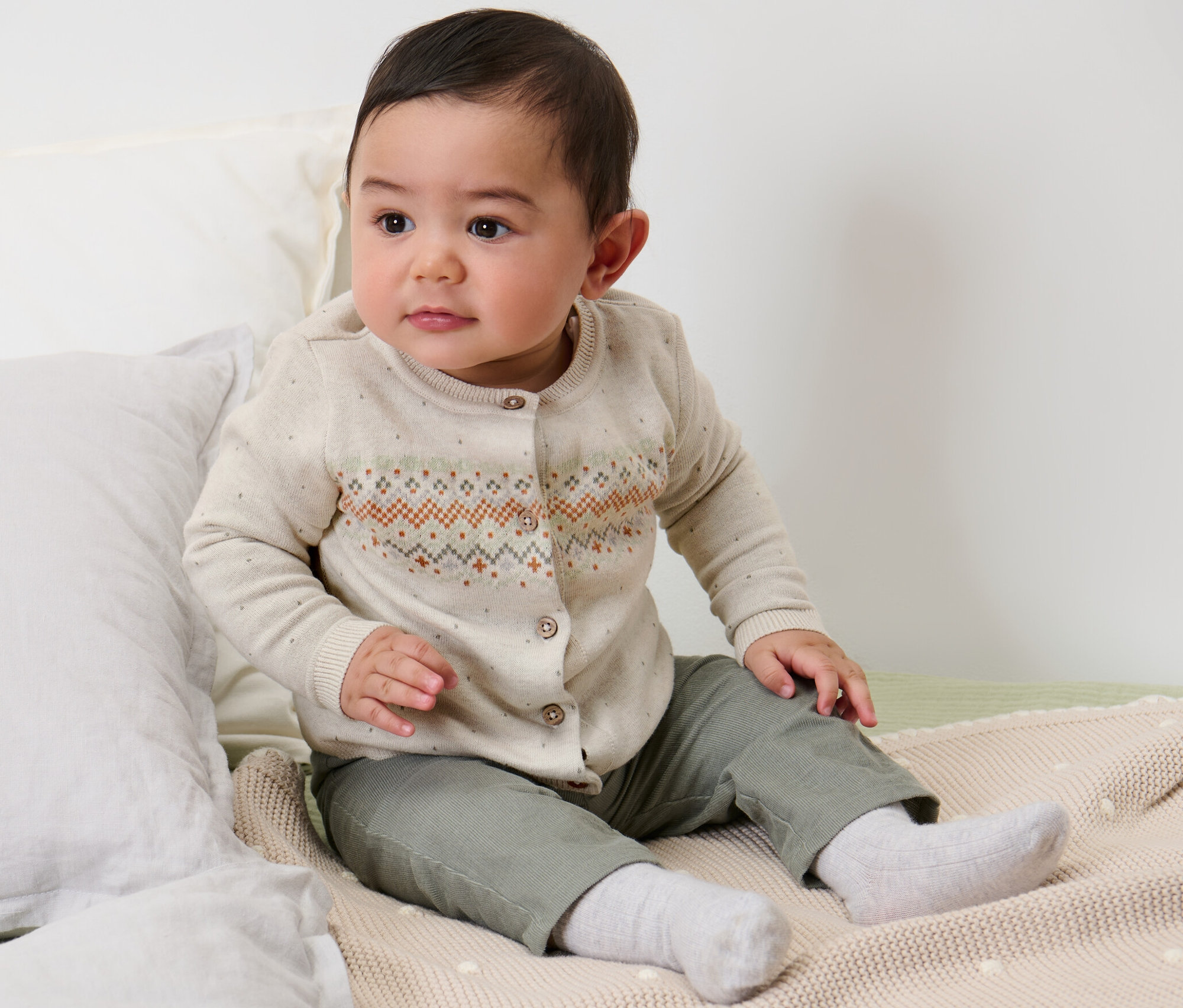 Un enfant est assis sur un lit et porte un gilet en maille pour enfant.