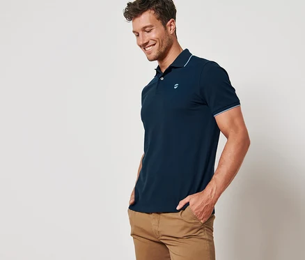 Un homme souriant pose en polo en piqué bleu marine.