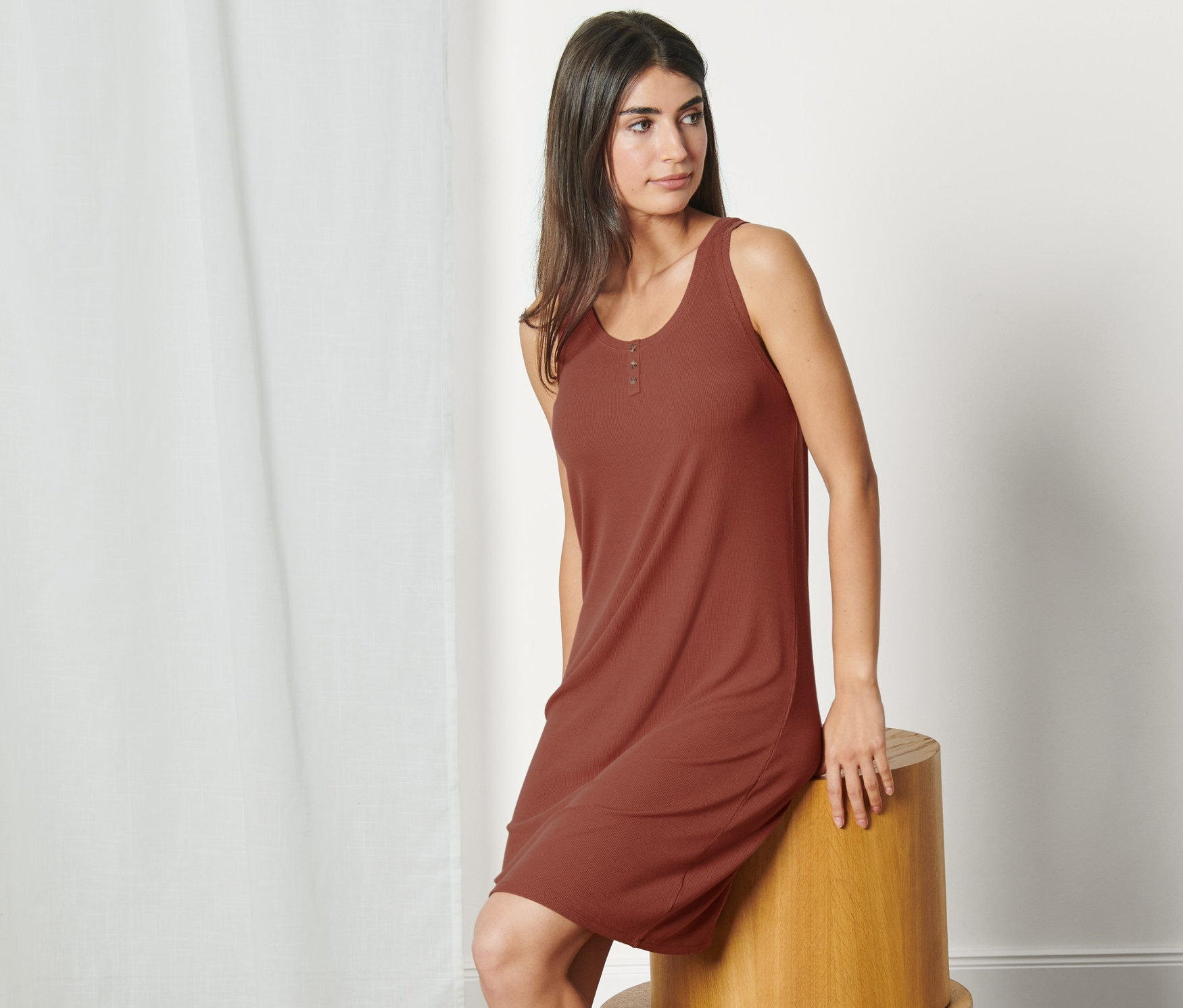 Une femme est assise sur un tabouret en bois et porte une chemise de nuit en matière côtelée.