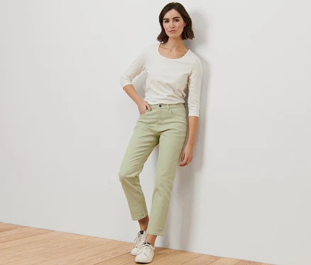 Une femme pose en jean moderne coloré – Fit « Ava » vert et un haut blanc.