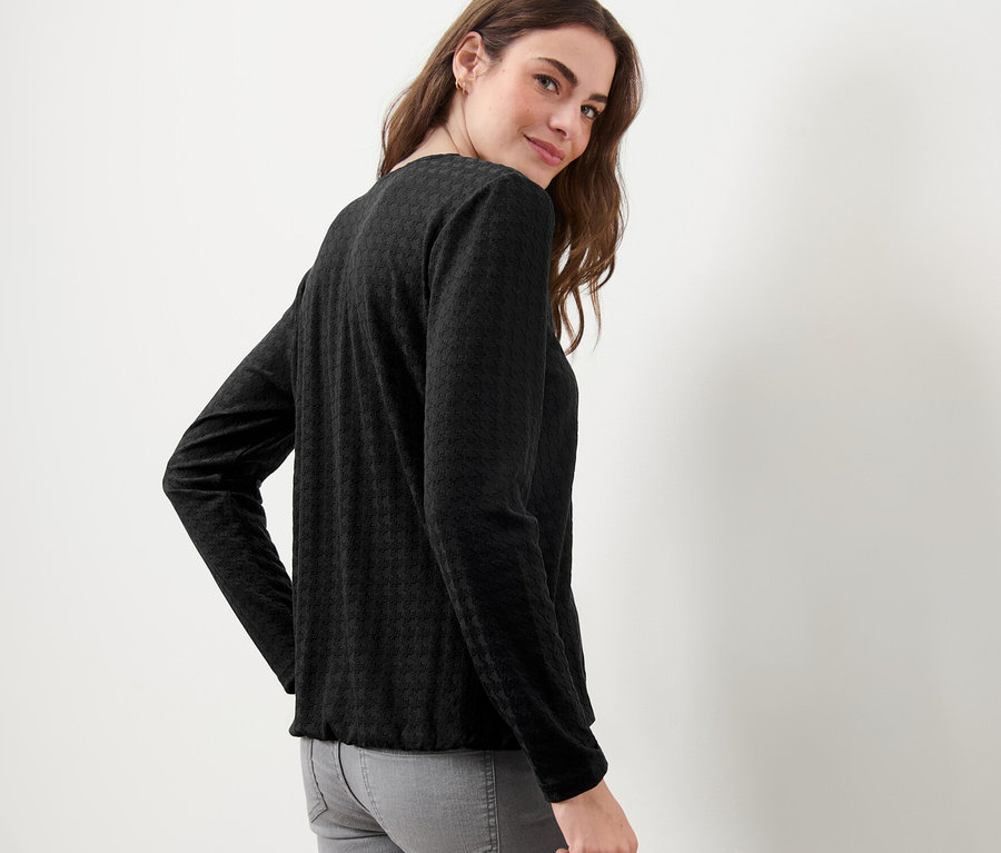 Une femme regardant par-dessus son épaule porte un t-shirt à manches longues structuré noir.