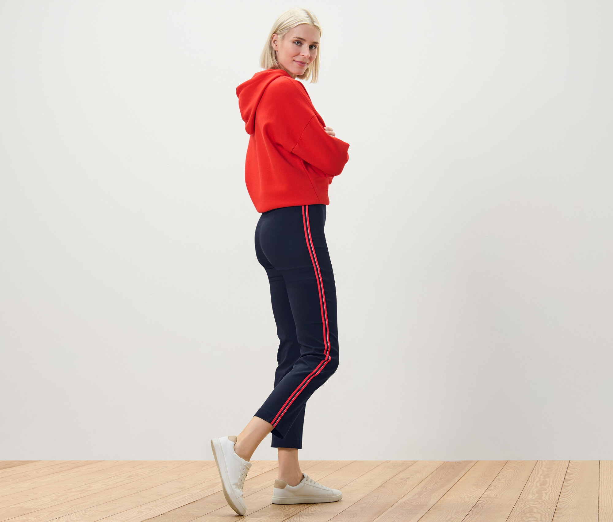 Femme blonde posant dans un sweat à capuche rouge et un pantalon stretch avec des galons.