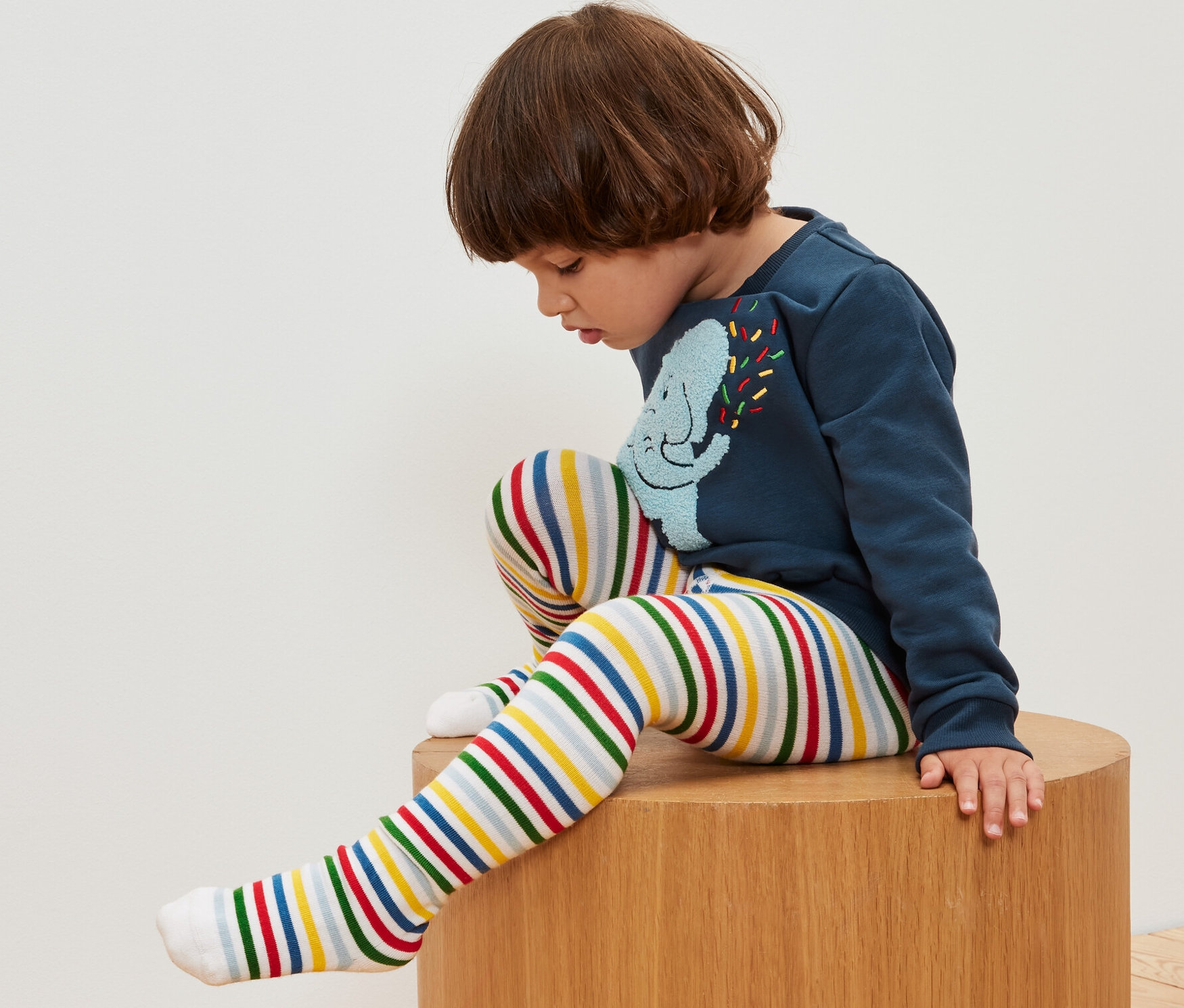 Un garçon est assis sur un tabouret en bois et porte des collants rayés. 5 paires de collants pour enfant.