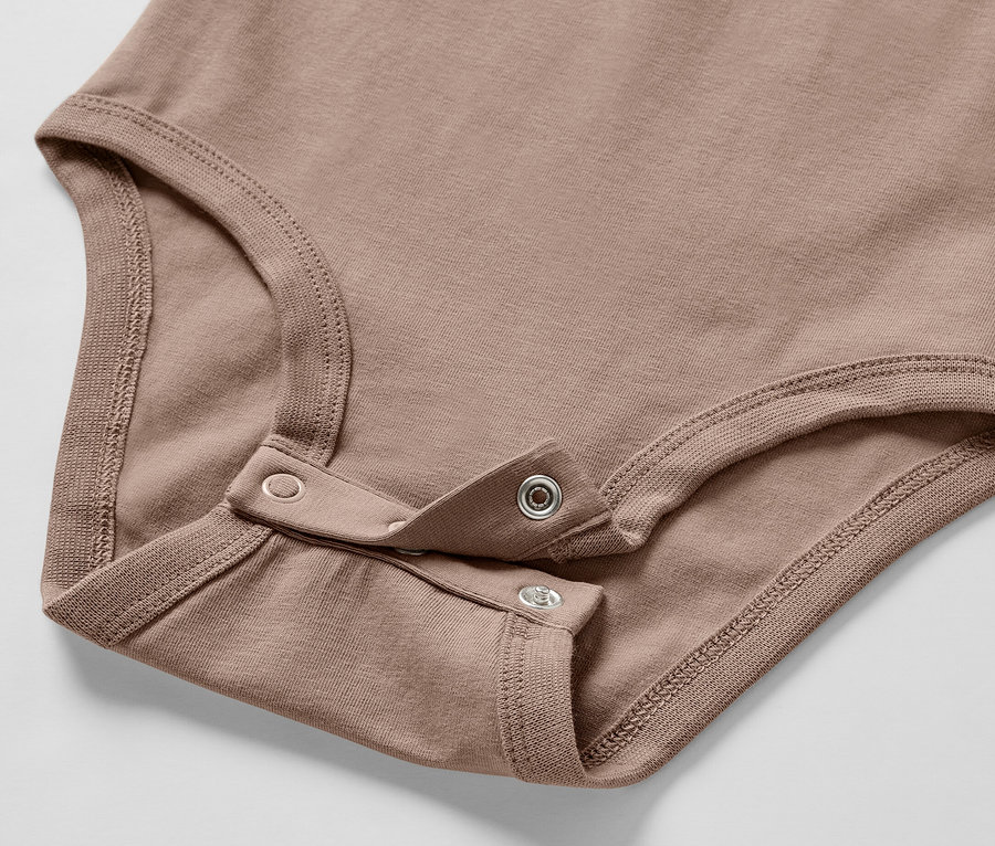 Gros plan sur un body marron pour bébé faisant partie d'un ensemble pour bébé, avec fermeture à bouton-pression.