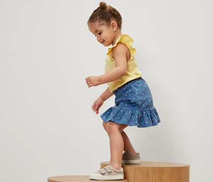Une fillette se tient sur un socle en bois et porte un t-shirt jaune et une jupe éponge pour enfants.