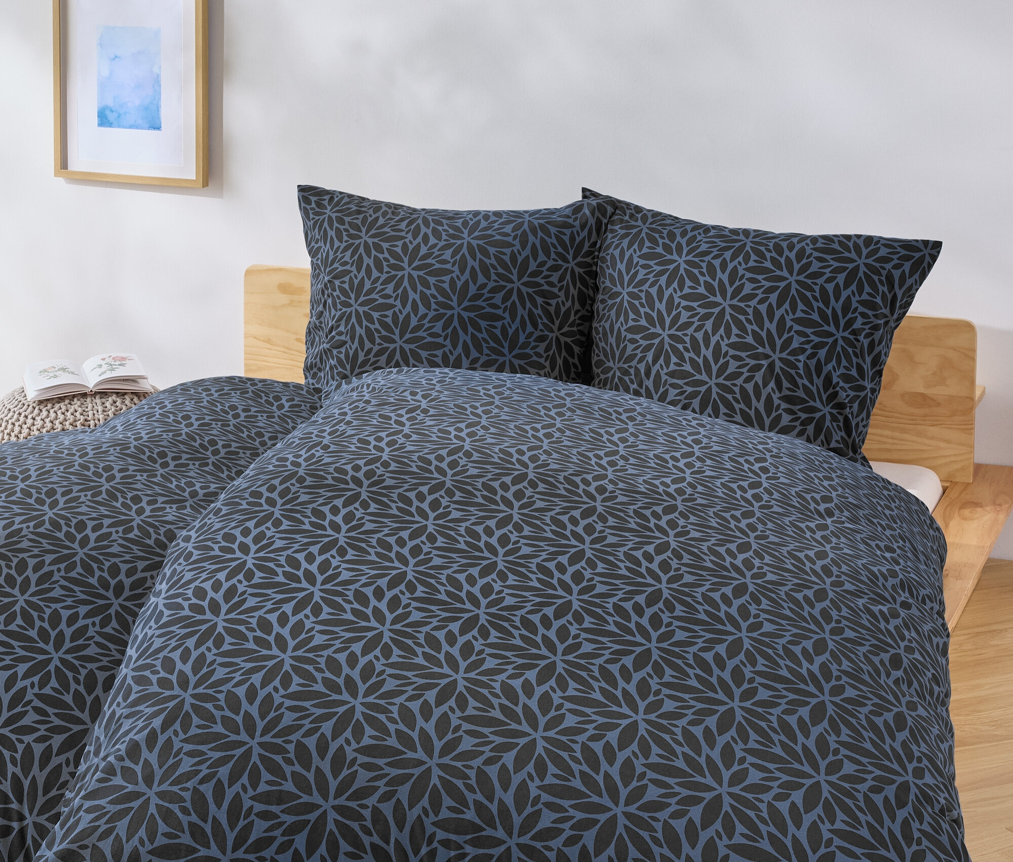 Lit avec une couverture à fleurs bleu et noir et deux oreillers.