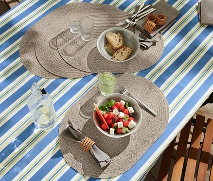 Table dressée avec 4 Sets de table essuyables ovales, salade, pain et boissons.