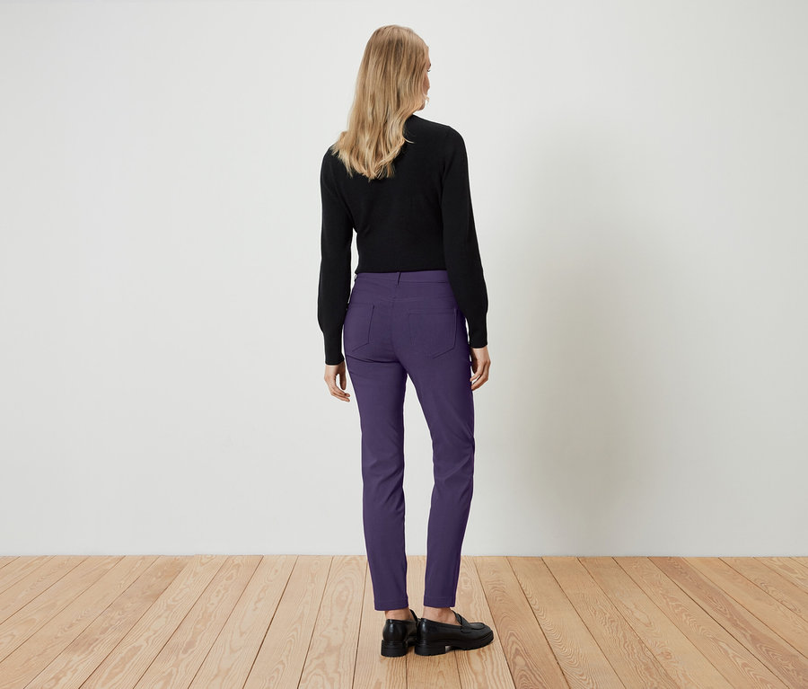 Une femme, vue de dos, porte un haut noir et un pantalon violet.