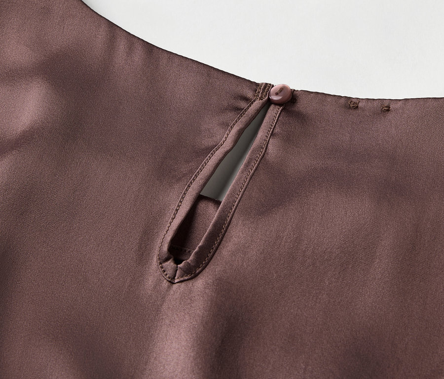 Détail d'un haut en satin marron avec une encolure en trou de serrure et une fermeture boutonnée dans le cou.